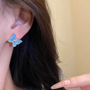 Close-up of elegant blue enamel butterfly stud earring worn on the ear of a model
