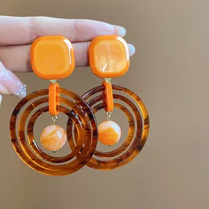 Close-up of retro geometric resin earrings in orange and amber Maillard tones
