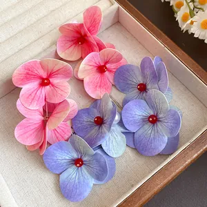 Detailed shot of pink and purple floral earrings with pearl accents and red beads