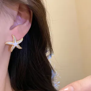 Close-up of a delicate gold starfish stud earring with white enamel on a model's ear.
