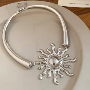 Detailed macro shot of a shiny silver sun pendant on a chunky metal choker necklace.