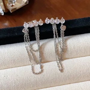 Macro view of silver-tone ear clips featuring '1314' numbers and heart charms with tassels