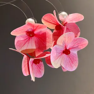 Close-up of pink fabric flower earrings with white pearl and red bead details