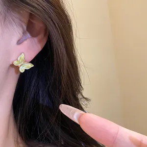 Detailed close-up showing a dainty yellow enamel butterfly stud earring on a model ear