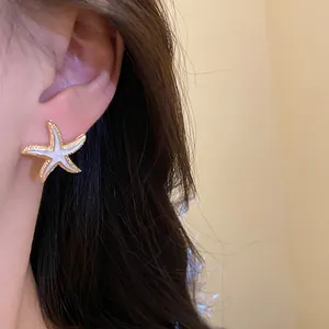 Detailed view of an elegant gold-tone starfish earring with white enamel inlay.