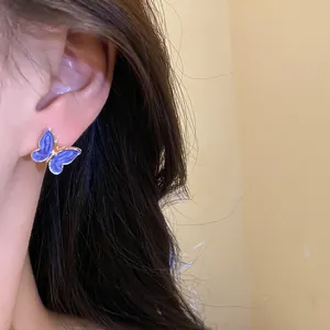 Detailed view of an elegant blue butterfly enamel stud earring worn on a model's ear