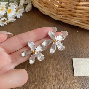 Macro detail of French-style silver brushed flower stud earrings with golden centers.