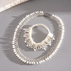 Détail du collier tissé en dentelle de perles blanches et perles de verre sur fond gris.