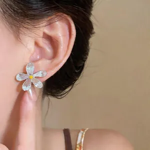 Detail shot of an elegant silver flower stud earring with a yellow center on a model