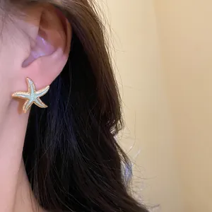 Close-up detail of a gold-toned starfish stud earring with light green enamel finish