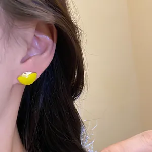Detailed view of a vibrant yellow enamel ginkgo leaf stud earring on a model's ear.