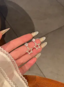 Detailed view of sparkling silver star dangle earrings with zircon studs held in hand.