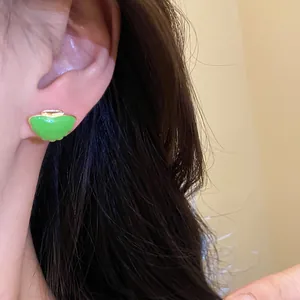 Close-up of vibrant green shell stud earring with gold edge worn on a person's ear