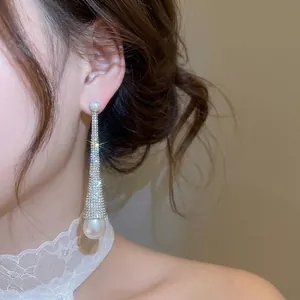 Luxurious long teardrop earrings with pavé crystals and white pearls worn by a model