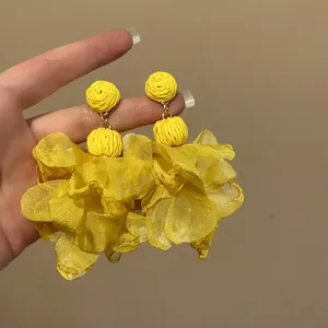 Close-up view of vibrant yellow chiffon petal earrings with woven ball detail