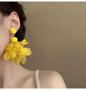 Close-up of oversized yellow chiffon petal earrings worn on an ear for a bohemian look