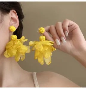 Detail shot of oversized yellow chiffon flower earrings with woven textures