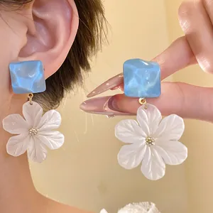 Close-up of elegant acrylic flower pendant earrings with blue square studs.