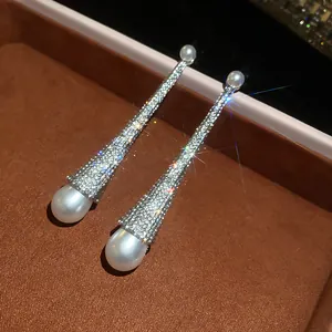 Close-up of long luxury drop earrings with sparkling pavé stones and white pearls