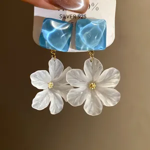 Close-up of translucent white acrylic flower drop earrings with blue square studs