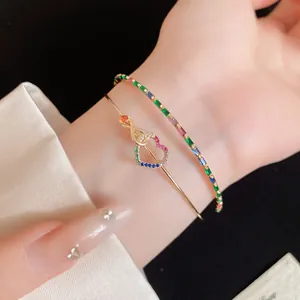 Détail d'un jonc cœur plaqué or 14K et d'un bracelet en strass colorés sur le poignet.