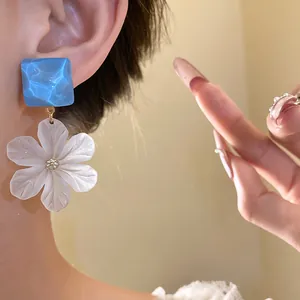 Close-up of translucent white acrylic flower drop earrings with blue square stud