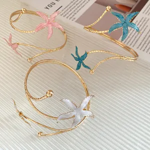 Bracelets de bras dorés élégants avec des étoiles de mer en émail coloré sur surface texturée.