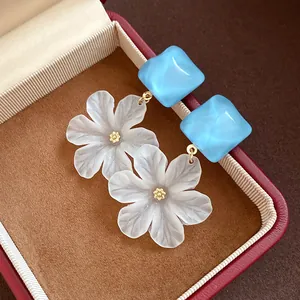 Detailed shot of frosted white flower acrylic drop earrings with blue square studs