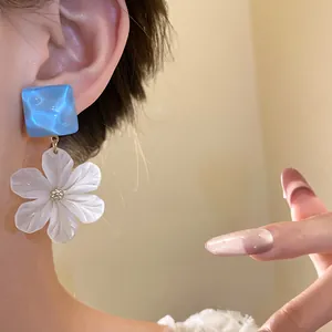 Close-up of elegant acrylic flower dangle earrings with a blue square stud detail