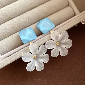 Close-up of frosted acrylic flower earrings with blue square studs in a box