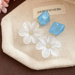 Macro detail of white acrylic flower earrings with blue geometric studs and gold center.