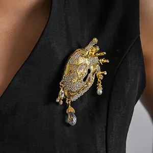 Detailed view of a gold anatomical heart brooch with rhinestones and pearls on black clothing
