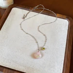 Close-up of a delicate silver chain necklace featuring a pink shell and green zircon pendant.