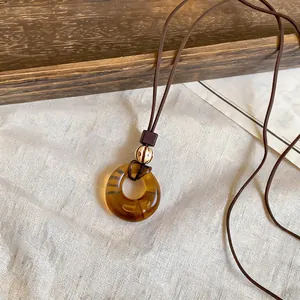 Macro detail of amber geometric resin ring pendant on a vintage brown cord necklace style