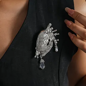 Close-up detail of a silver anatomical heart brooch featuring crystals and pearls on clothing.