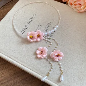 Dettaglio di una collana girocollo con fiori rosa, perle e un elegante pendente a nappa