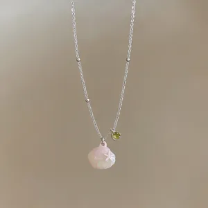 Detailed view of pink shell pendant and green gemstone on silver beaded chain necklace.