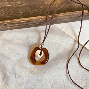 Detail view of a Maillard-style amber resin pendant necklace with soft fabric background.