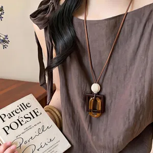 Detail view of a vintage amber geometric resin pendant long necklace on a brown cord