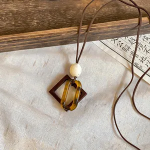 Close-up of retro Maillard style amber resin and wood geometric pendant necklace.