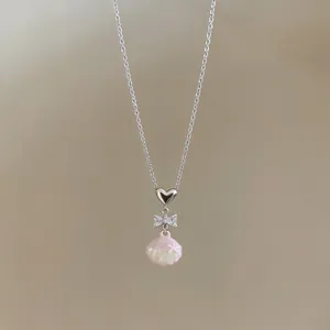 Close-up of stainless steel heart necklace with zircon bow and pink shell pendant.