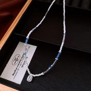 Close-up of pearl necklace with blue beads and a clear crystal pendant in a black box