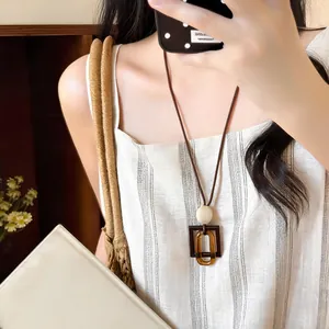 Vintage Maillard style amber geometric resin long pendant necklace worn by a model in a mirror
