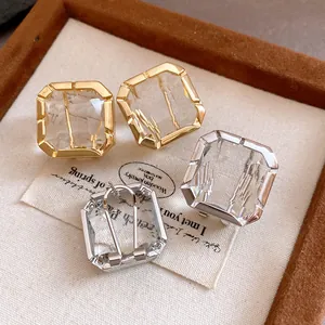 Close-up detail of elegant square crystal stud earrings in both gold and silver tones
