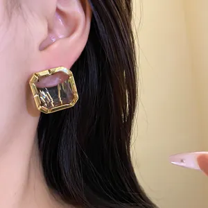 Detailed view of elegant square crystal earrings with a gold frame on ear.