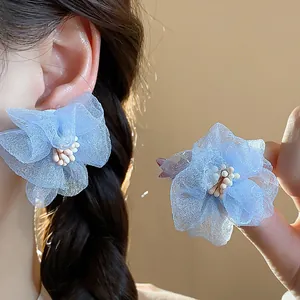 Dettaglio di orecchini a lobo con fiori in chiffon azzurro e petali delicati.