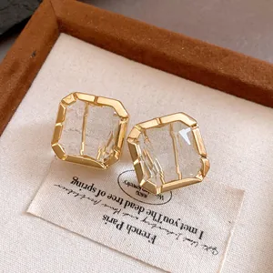 Close-up detail of elegant square gold-toned earrings featuring clear faceted crystals.