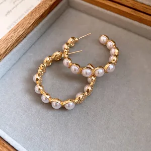 Détail de boucles d'oreilles créoles dorées en C avec perles dans un écrin en velours