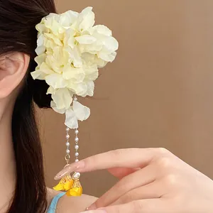 Detailed view of cream fabric flower hair clip with pearl tassels and yellow charms