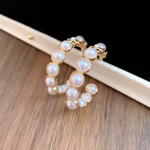 Détail rapproché de boucles d'oreilles créoles dorées en C avec perles et strass brillants